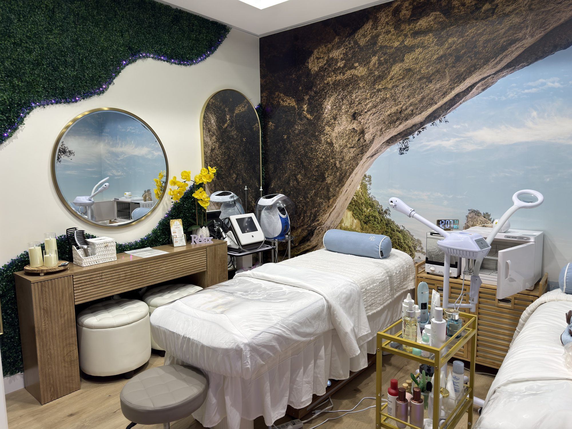 Bright treatment room with a nature mural, draped bed, round mirror and equipment trolley